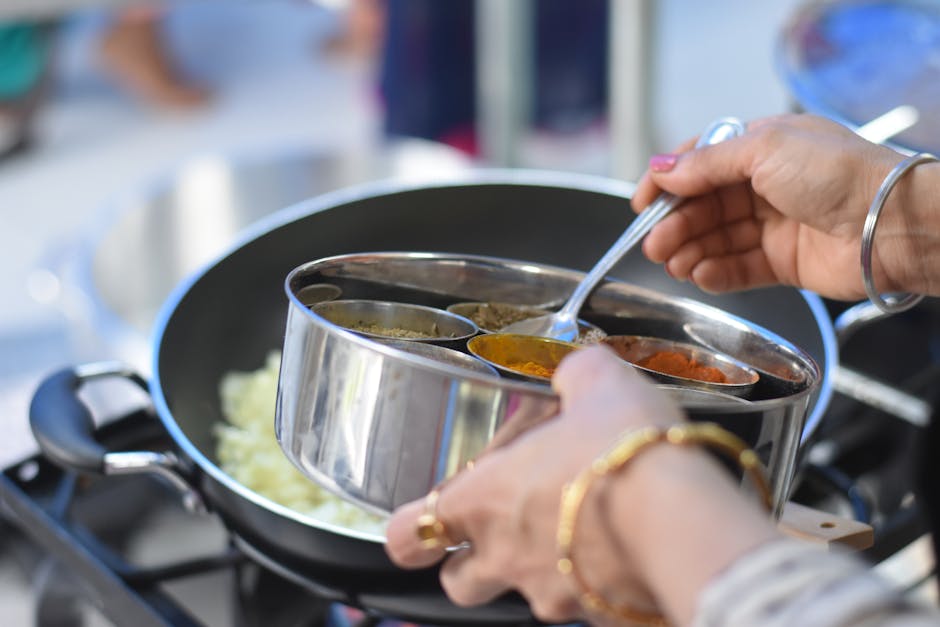 Close-up of hands preparing Indian dish with spices in a cooking pan.